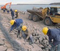 En los trabajos intervienen unos 100 operarios. Hay tramos del enrocado que se colocan con una retroexcavadora y otros, a mano. En las cotas superiores de la presa se colocan gaviones, algunos con basalto y otros, con piedra bocha. A las compuer-tas del vertedero les soldaron nuevos tramos.