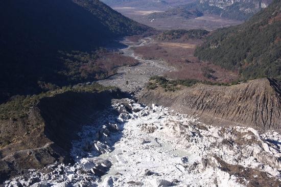 Una persona muestra la proporción con los enormes trozos de hielo que rodaron. Los hielos y el agua acumulados rompieron la ladera de un cerro y arrasaron con todo. 